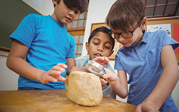 3 kids looking at a rock through a magnifying glass