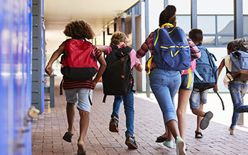 Students running in the hallway wearing schoolbags. Viewed from behind