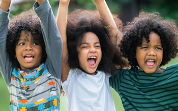 Happy boy and girls playing in the playground in school with their hands in the air.