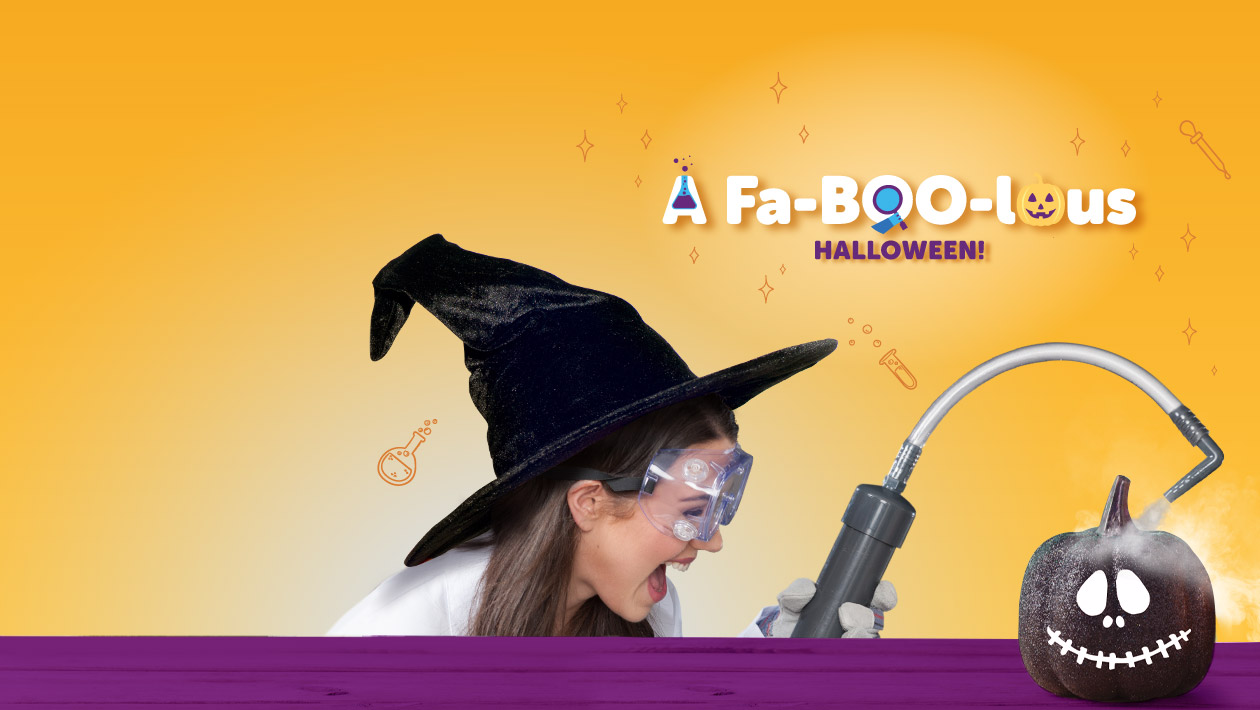 A mad science instructor wearing a witch hat using the mad science smoke shower machine over a black pumpkin.